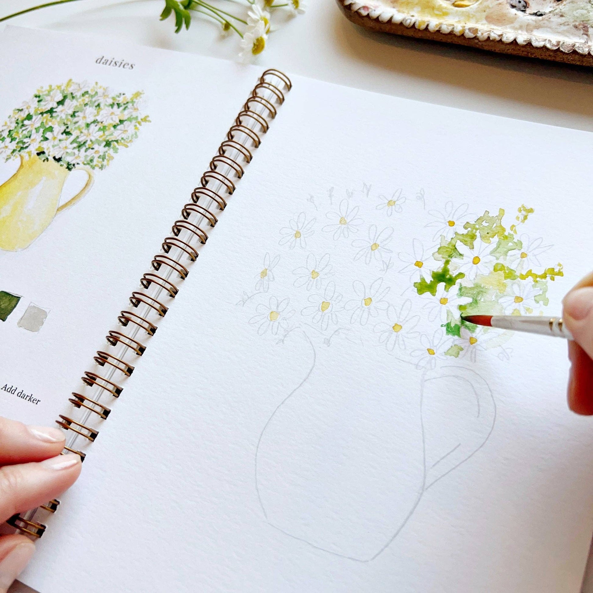 Person drawing flowers in a notebook with a pen