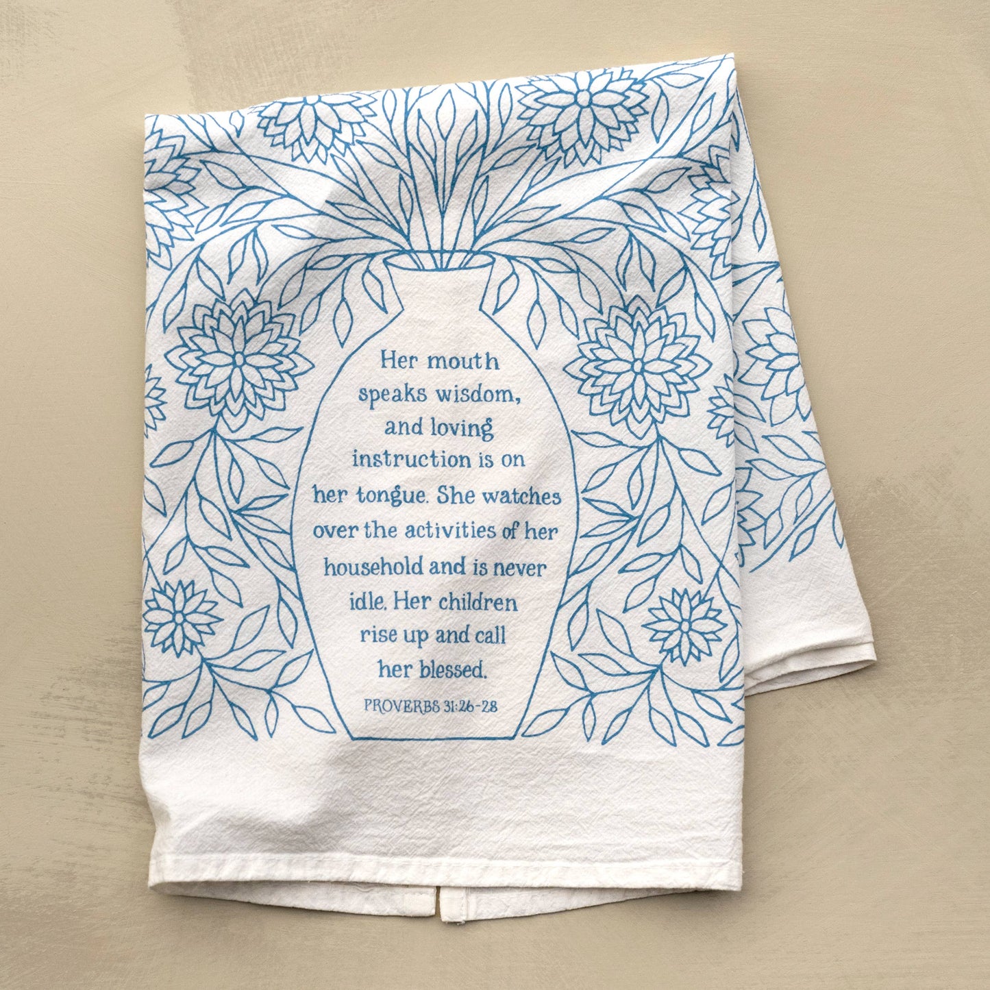 Flat lay of Proverbs 31 tea towel in light blue with scripture on wooden kitchen surface