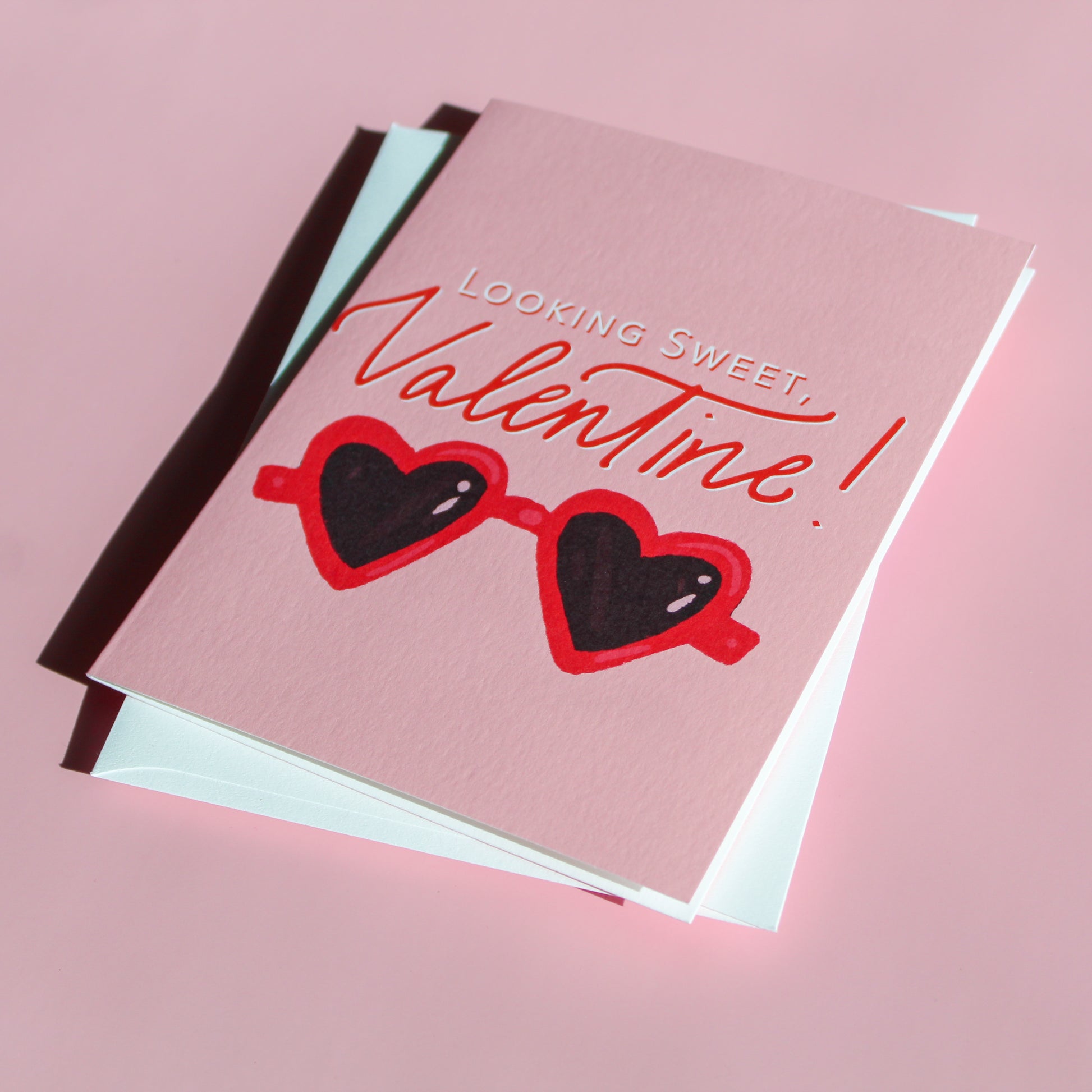 Our "Looking Sweet, Valentine!" Valentine's Day card features hand drawn heart sunglasses on a pink background - it is perfect for a kid or adult! Each card is folded to 4.25" tall by 5.5" wide, is blank inside and comes with a matching white envelope. Cards are packaged in cellophane sleeves.