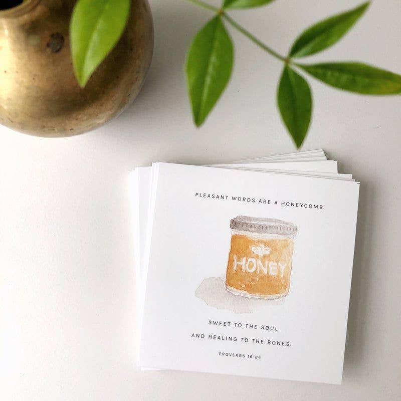 Card with honey jar illustration and text on a white surface with green leaves