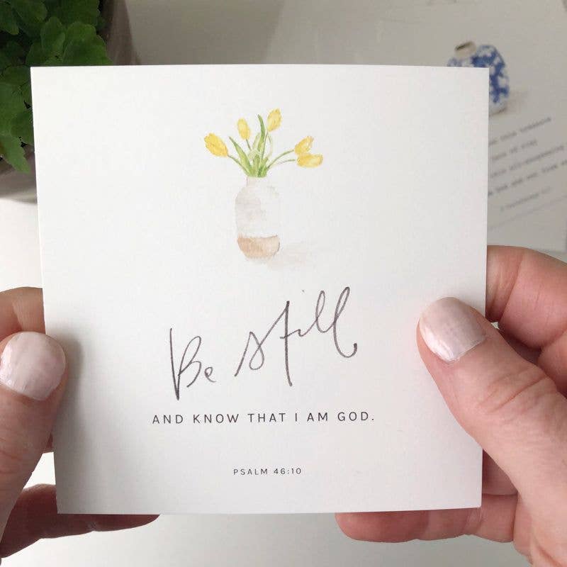 Card with floral design and 'Be Still and Know That I Am God' text held by a person.