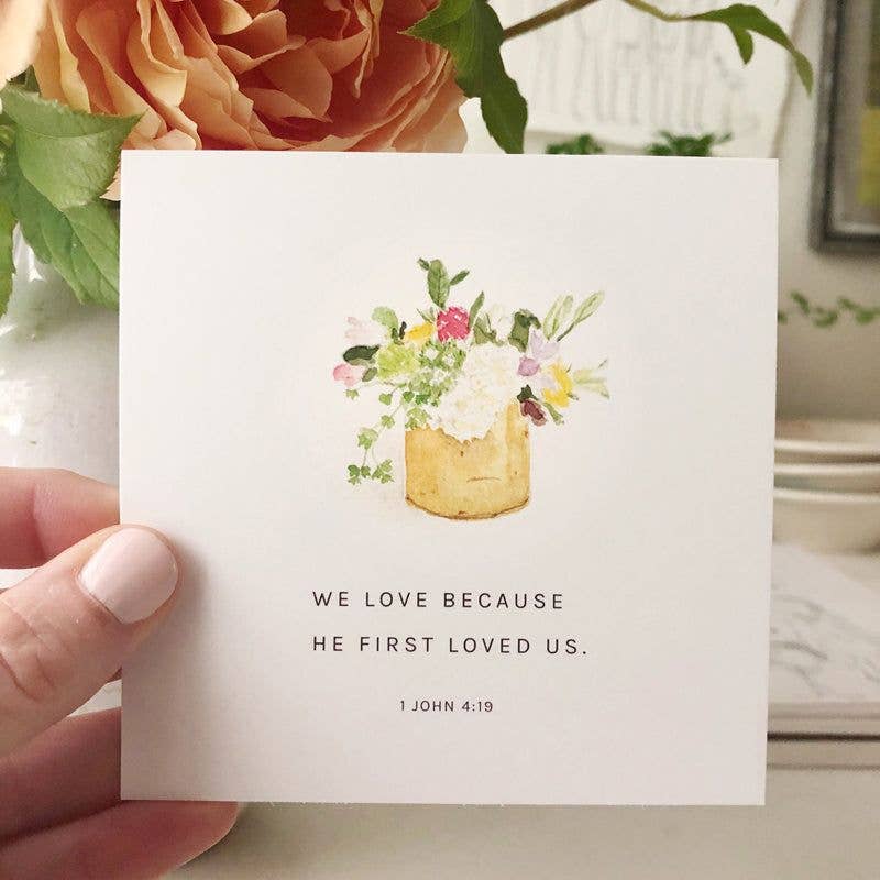 Card with floral illustration and text held by a hand, with flowers in the background