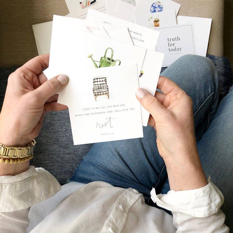 Person holding a card with illustrations of furniture and text, sitting on a couch with more cards in the background.