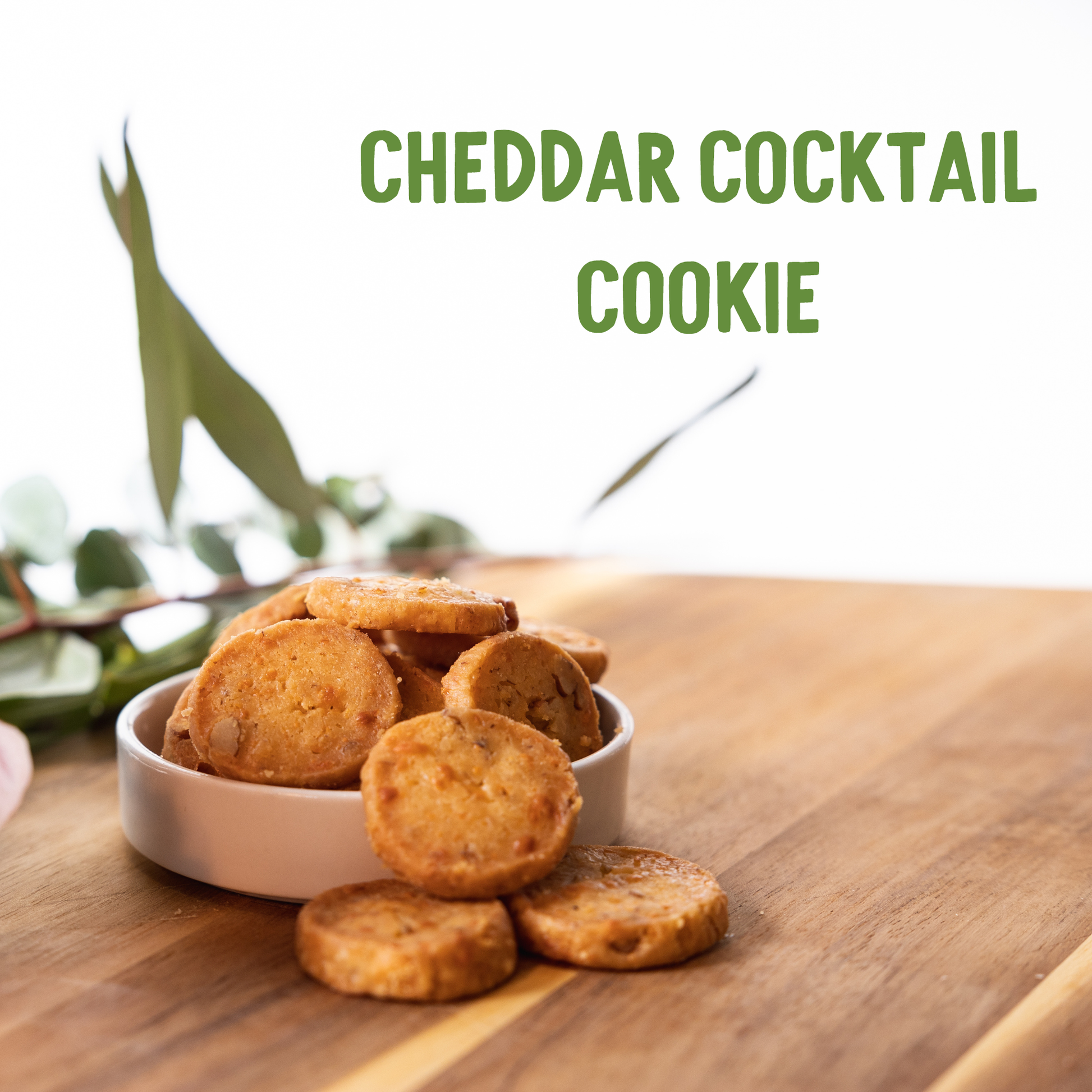 Whatanut Cheddar cocktail cookies in a bowl on a wooden surface with greenery in the background